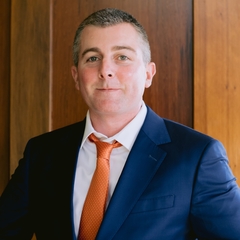 man with short hair wearing a blue suit and orange necktie